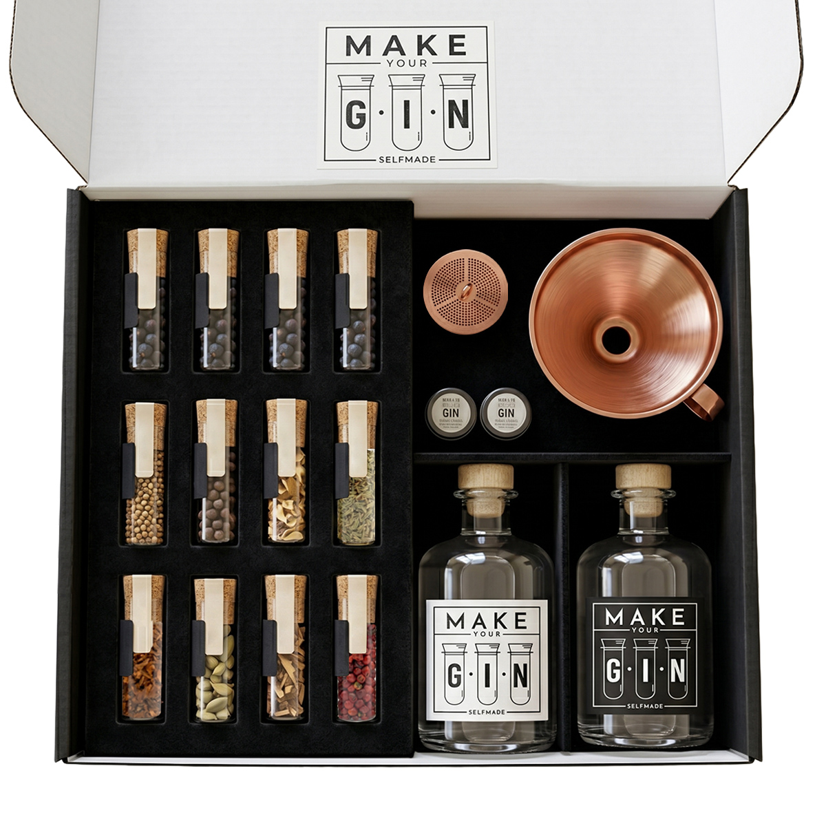 Das „Make Your Gin“-Set ansprechend arrangiert auf einer dunklen Steinoberfläche. Neben der Flasche und dem Trichter liegen verstreute Kaffeebohnen, Safranfäden und Wacholderbeeren zur Dekoration.